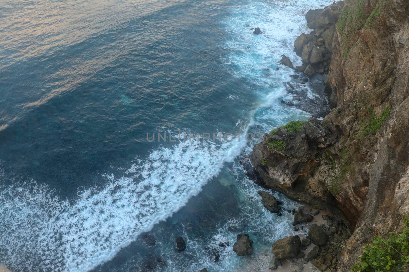 Overview panorama ocean shore, cliff. Sunset. Bali. Overwhelmed scene the flower and green-capped vertical cliff over the Indian ocean. South of Bali island, Pura Luhur Uluwatu Temple. Indonesia.
