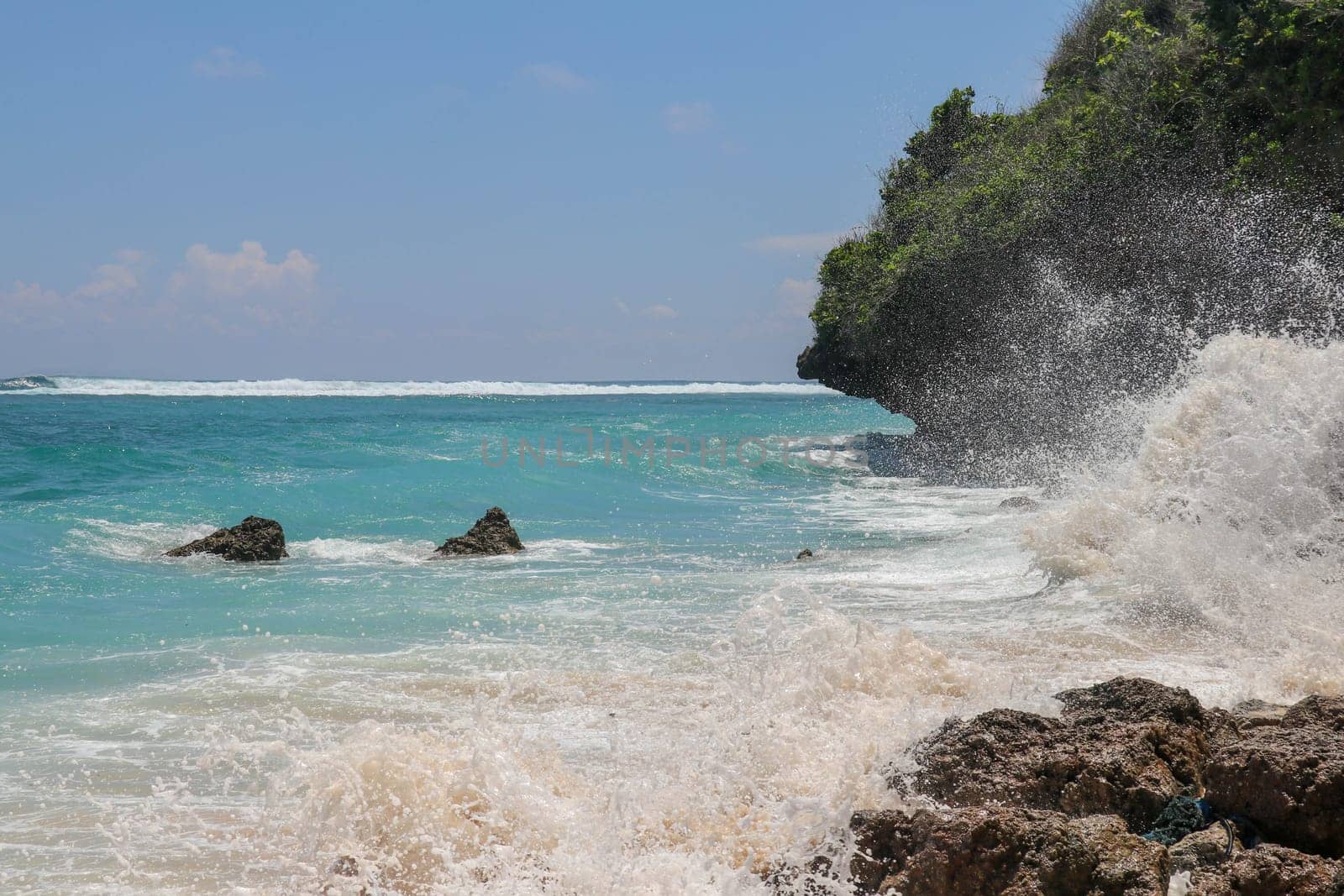 Pantai Gunung Payung beach with fine golden sand, Bali. Turquoise blue water turns into sea foam as the waves break against rocky cliffs of the coast. Sunny day with blue sky. Tourist natural concept.