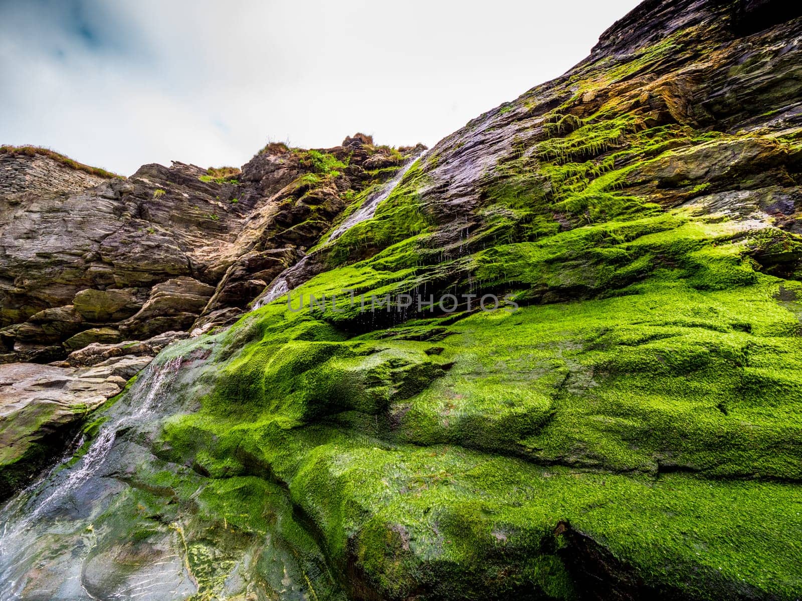 Beautiful waterfall over mossy stones in the Cove of Tintagel in Cornwall