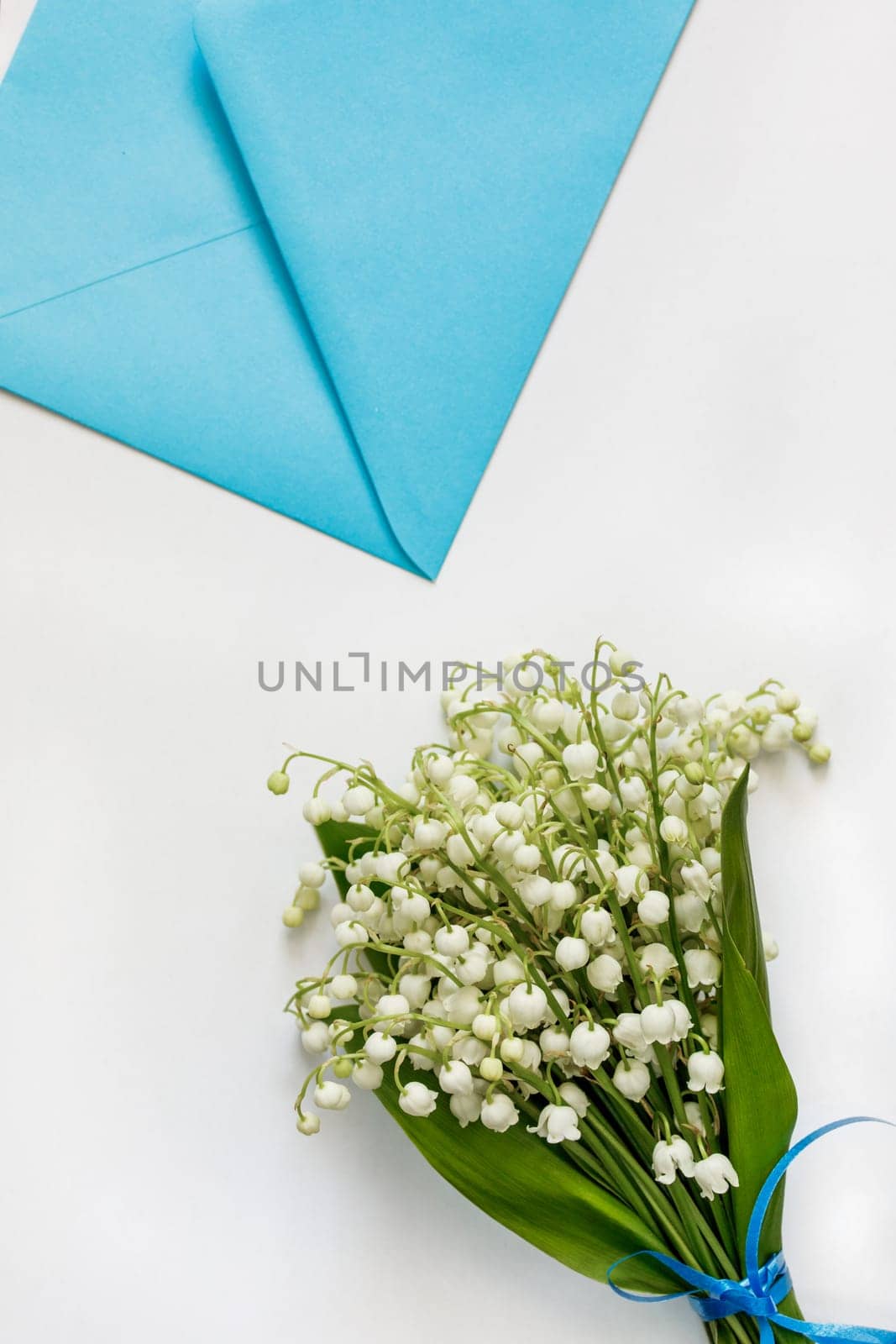 Bouquet of lilies of the valley and a blue envelope on a white table