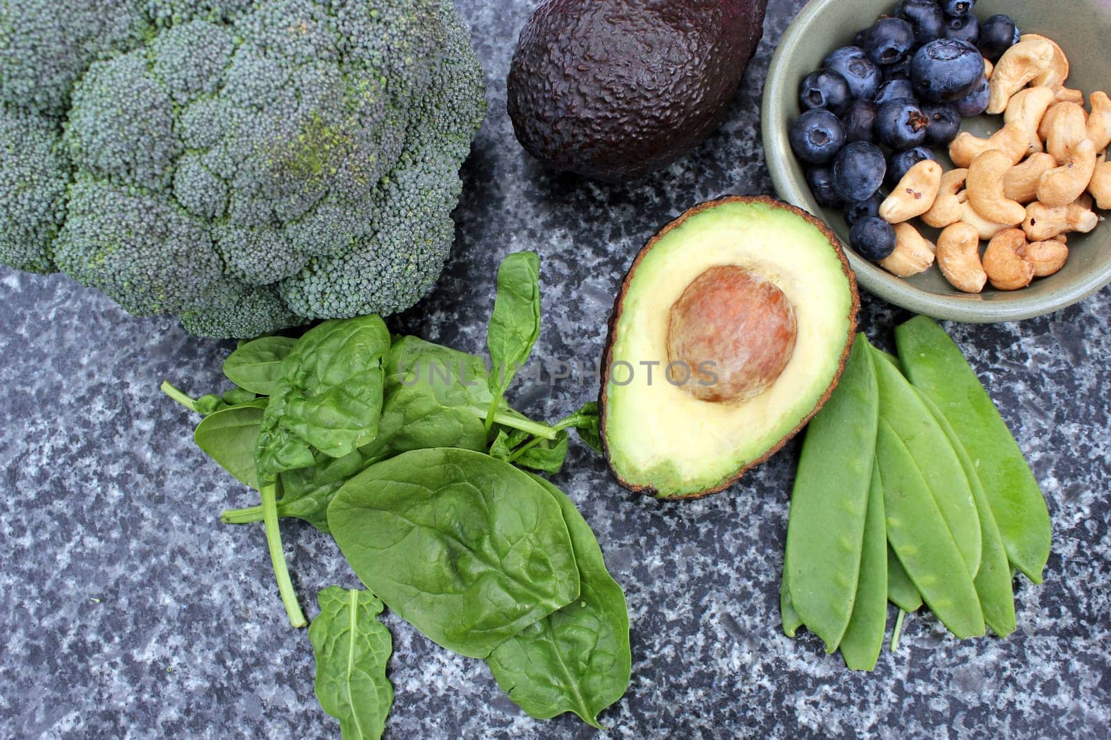 Vegan vegetarian plant based diet gluten free selection of cashew nuts, blueberries, spinach, mange tois peas avocado and broccoli on marble and board background