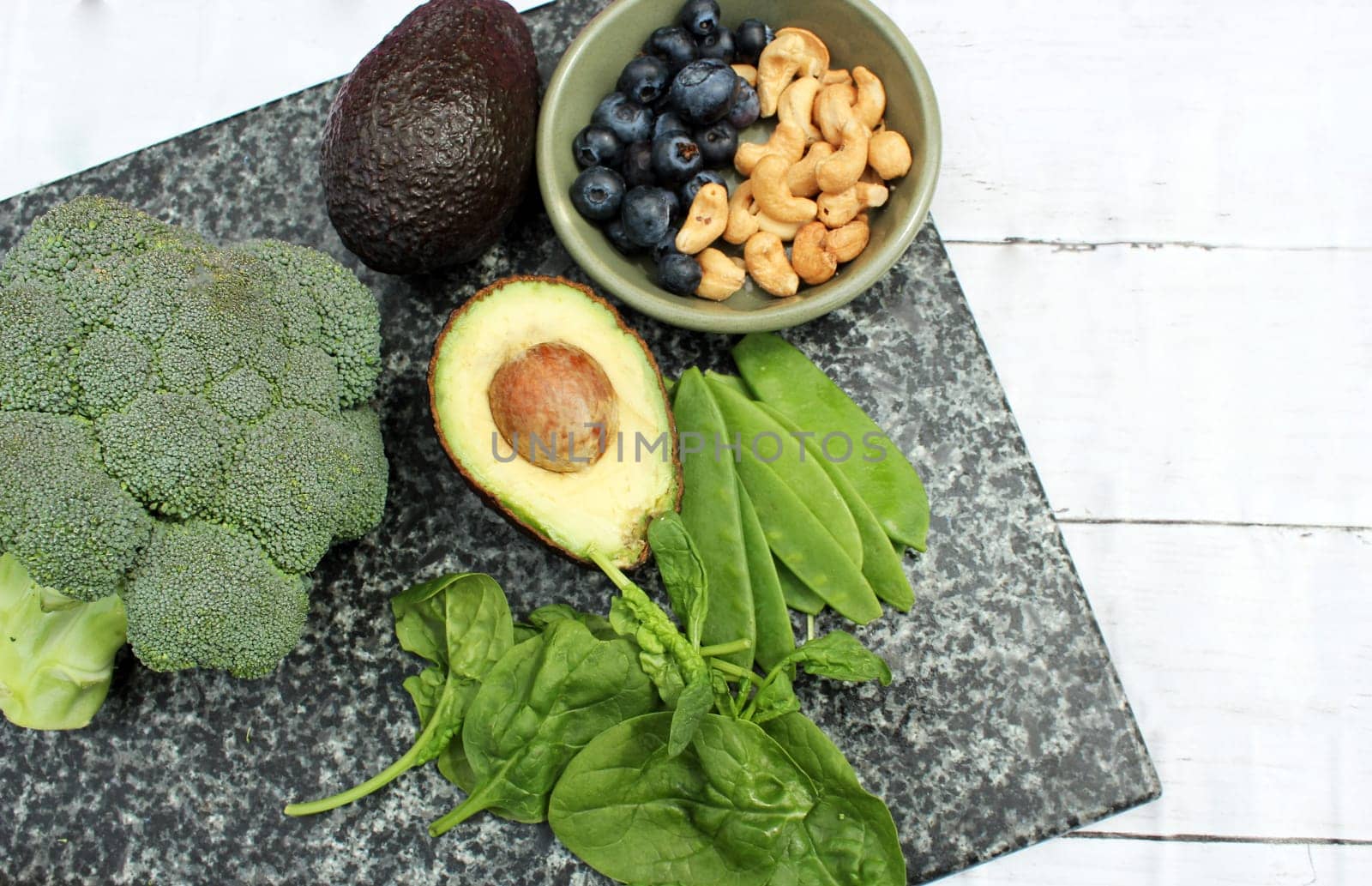 Vegan vegetarian plant based diet gluten free selection of cashew nuts, blueberries, spinach, mange tois peas avocado and broccoli on marble and board background