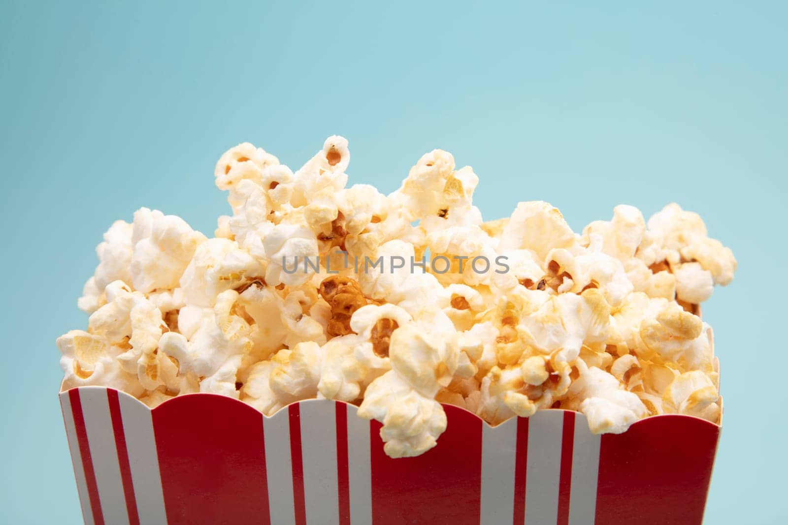 Large paper cup filled with salted Pocorn on bright blue Background