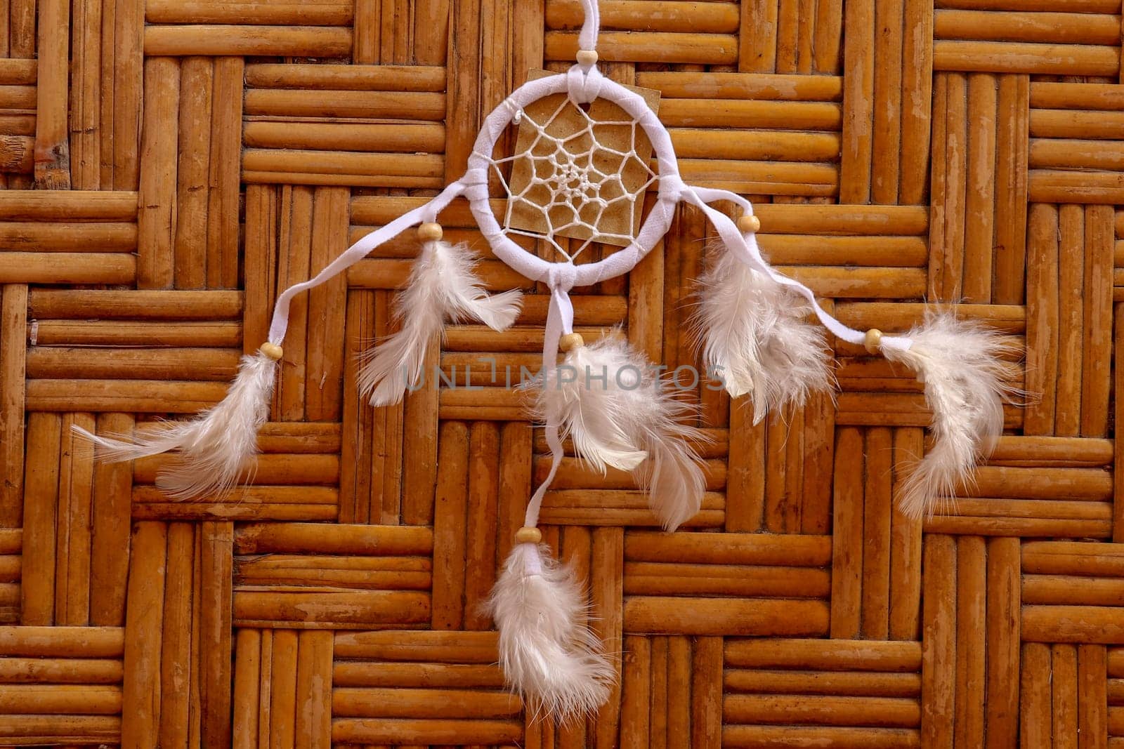 Dream catcher, decorated with white feathers and wooden beads, on a wooden surface. Dream catcher with wooden circle. Knitted Native American amulet with the symbol of Yin Yang on a wodden background.