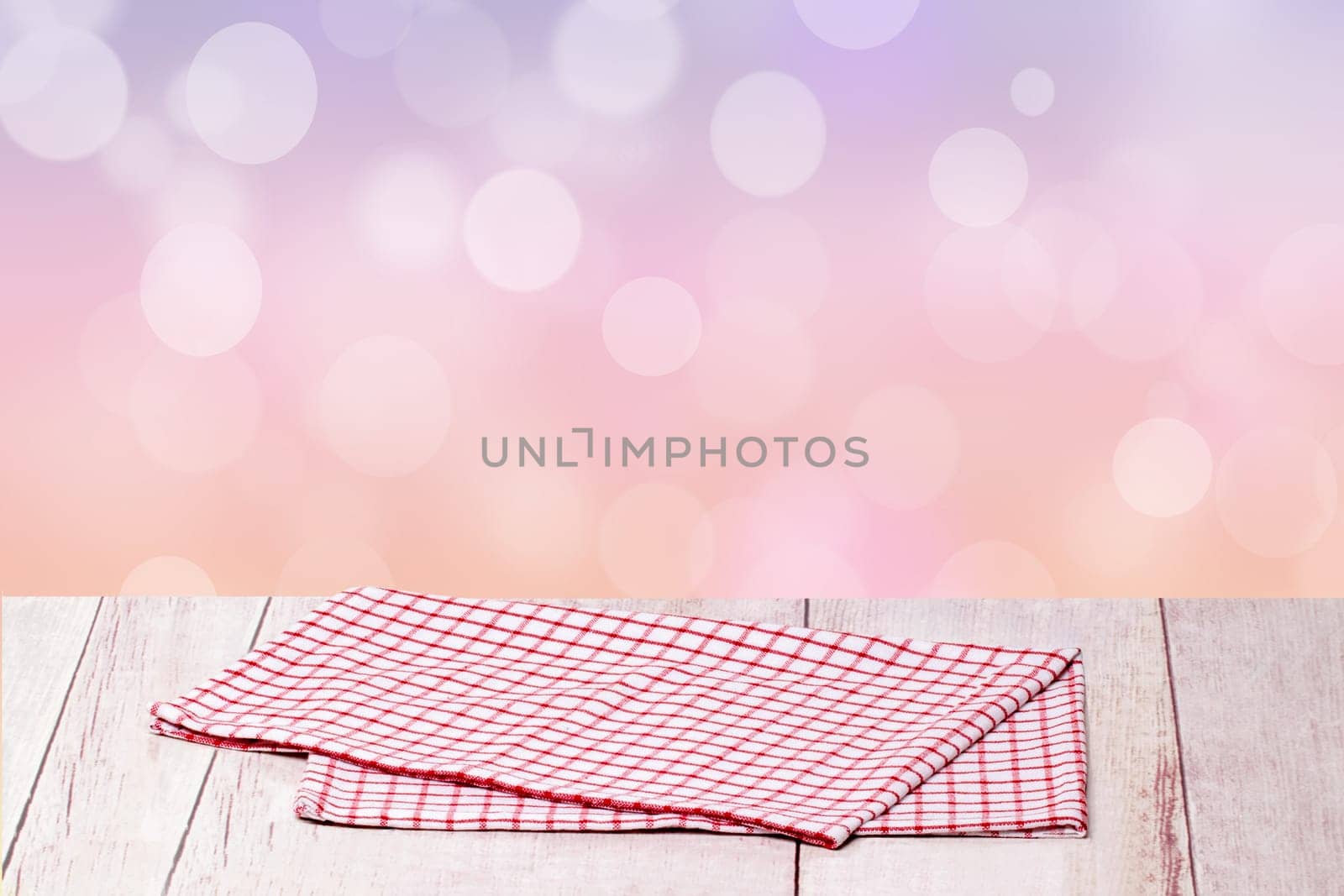 Empty table product. Closeup of a empty red checkered tablecloth or napkin on a rustic bright table over abstract pastel pink background. Template for your food and product display montage.