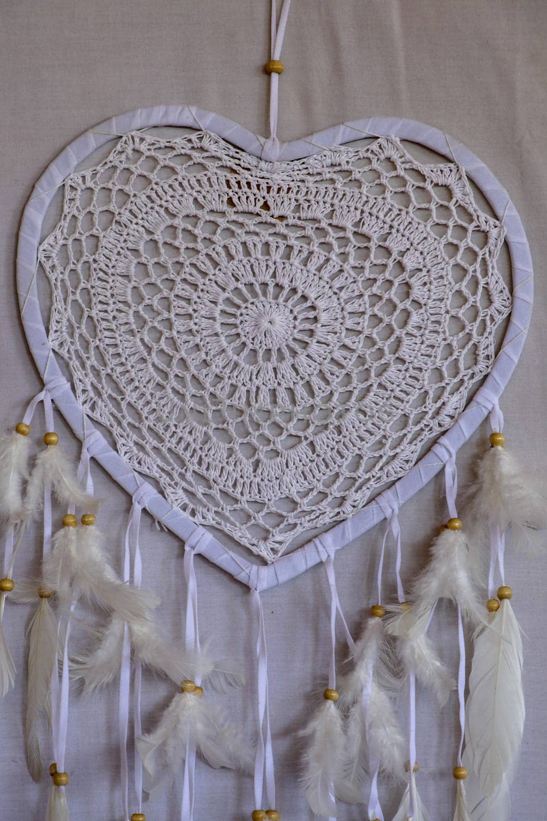 Dream catcher shaped heart with beige peacock feathers in the interior.