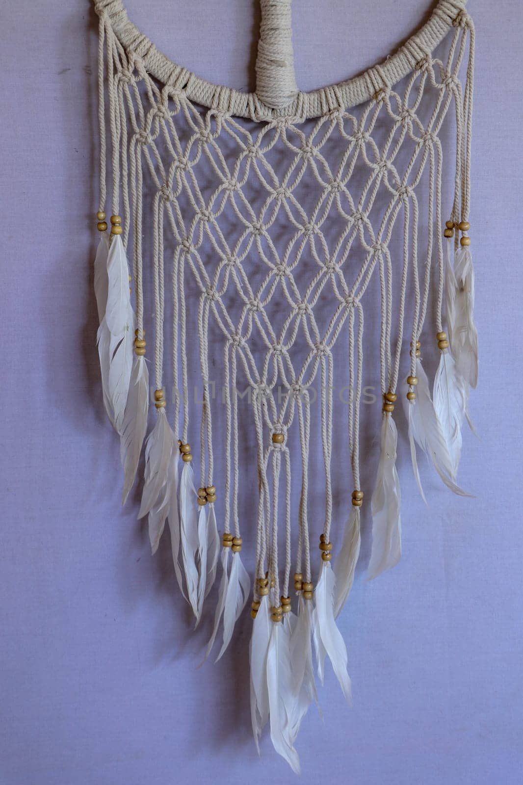 Handmade pink dream catcher with white doily on background of rocks and lake. Tribal elements, feathers, lace, crochet snowflake.