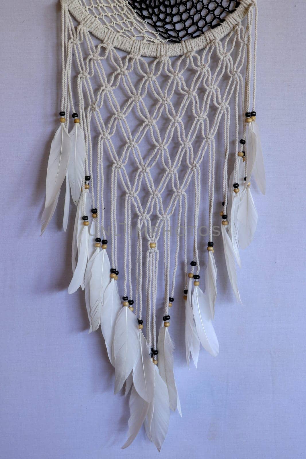 Handmade pink dream catcher with white doily on background of rocks and lake. Tribal elements, feathers, lace, crochet snowflake.