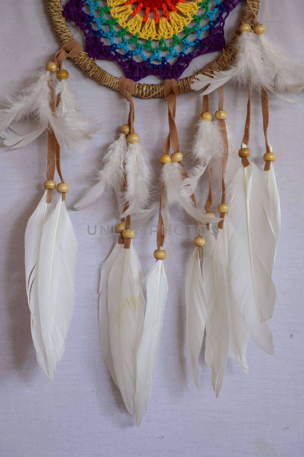 Handmade pink dream catcher with white doily on background of rocks and lake. Tribal elements, feathers, lace, crochet snowflake.