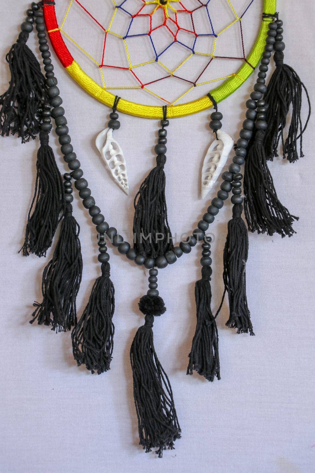 Handmade pink dream catcher with white doily on background of rocks and lake. Tribal elements, feathers, lace, crochet snowflake.