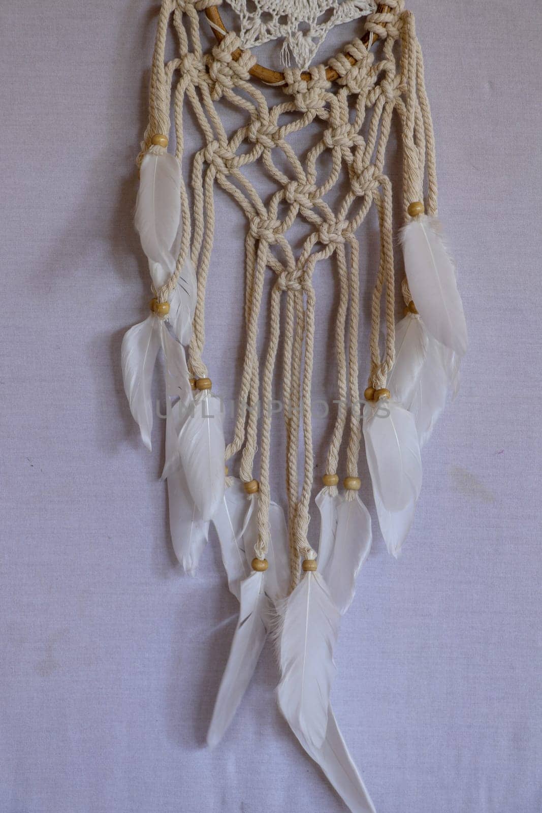 Handmade pink dream catcher with white doily on background of rocks and lake. Tribal elements, feathers, lace, crochet snowflake.