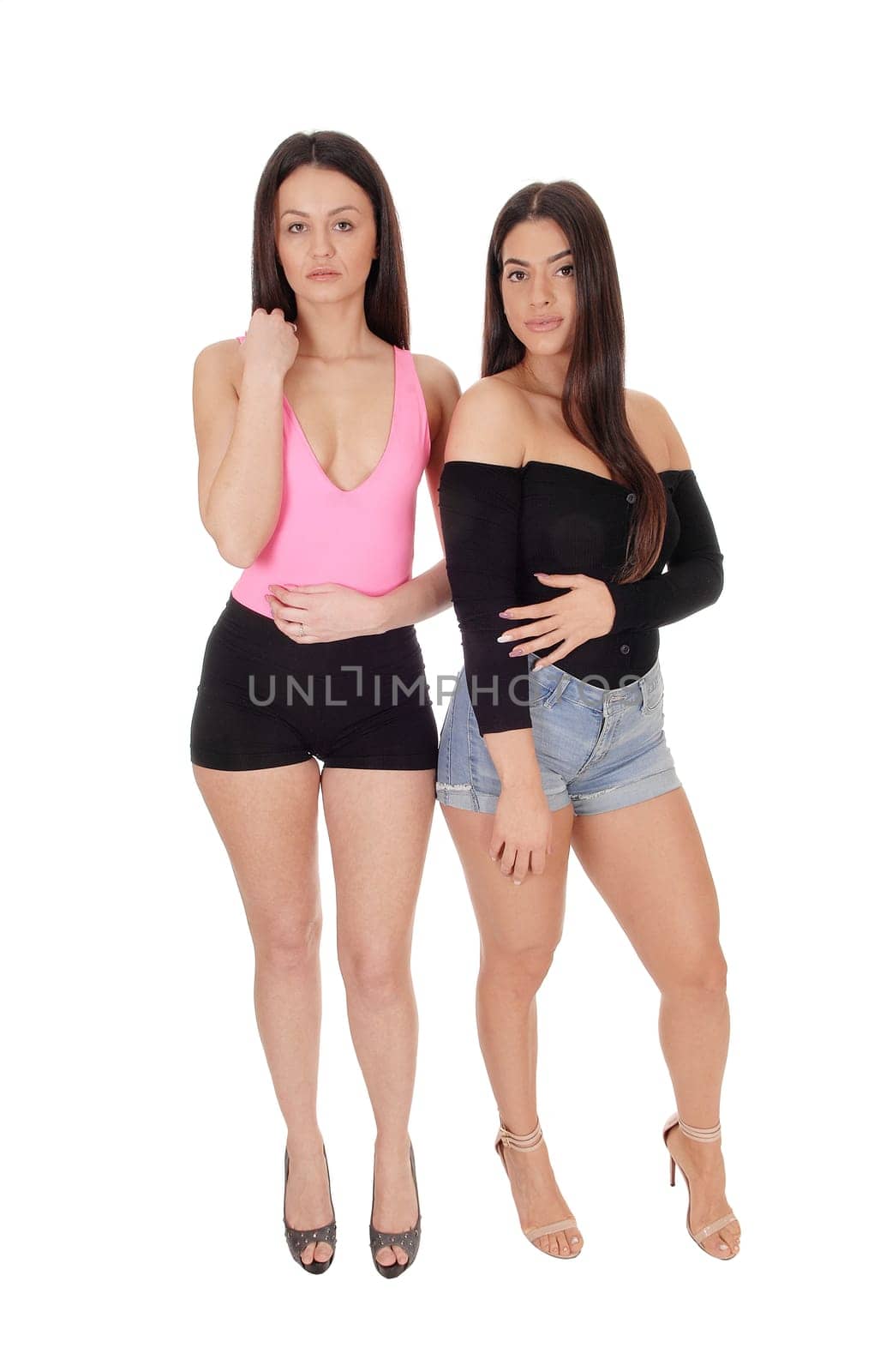 A two happy young slim women standing in the studio in shorts .side by side, looking at camera, isolated for white background.