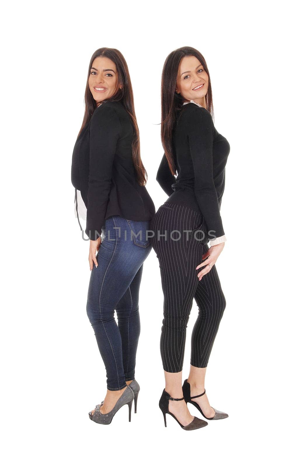 Two beautiful young woman standing back to back in jeans and heels.looking at the camera, isolated for white background.
