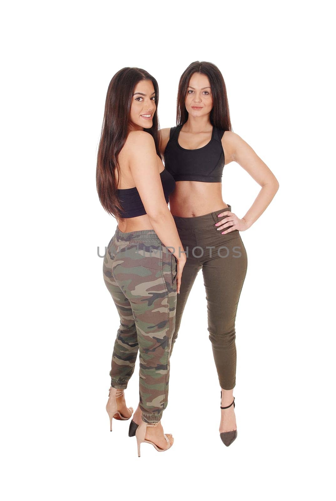 Two beautiful young woman standing face to face in jeans and heels.looking at the camera, isolated for white background.