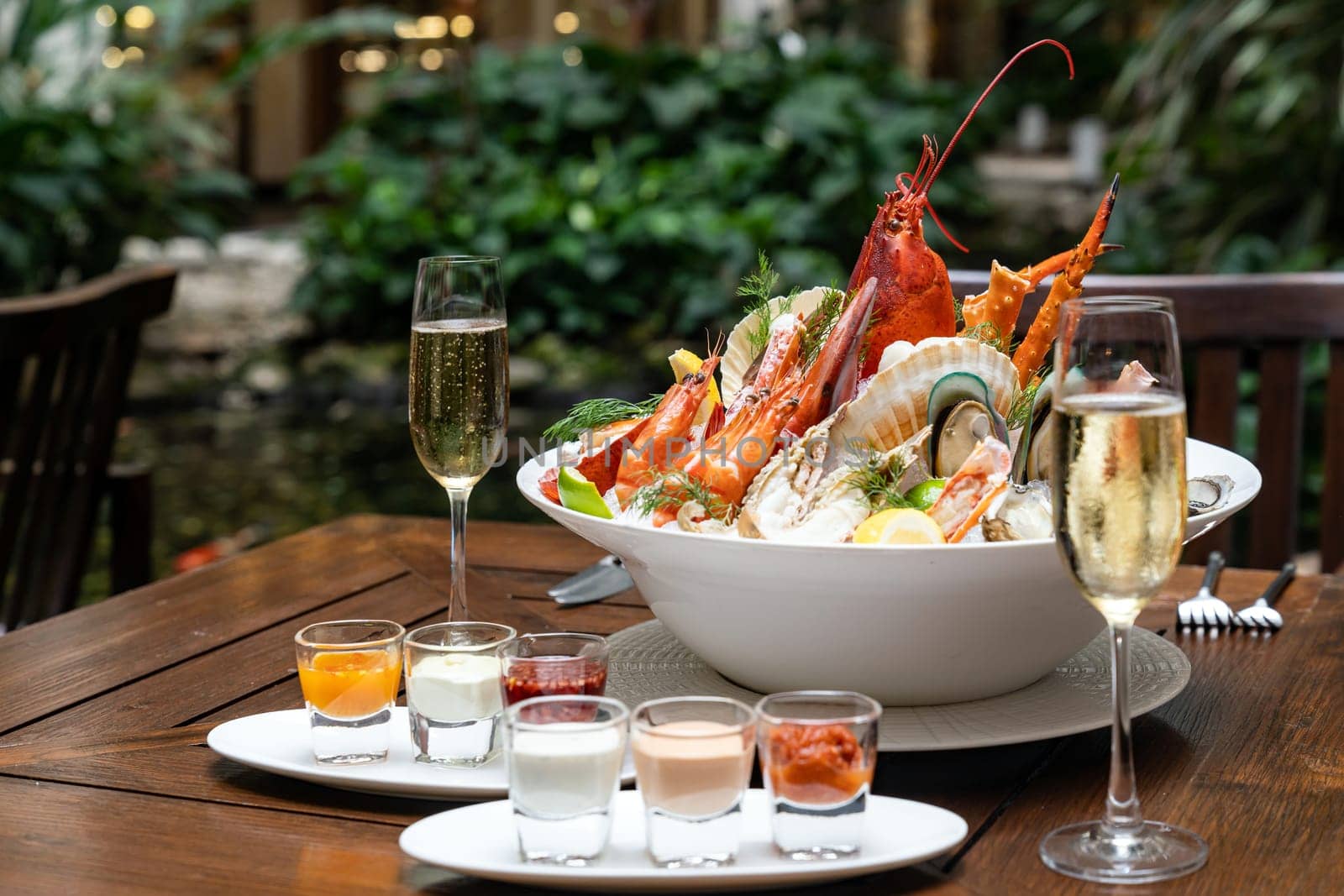 Bowl of gourmet fresh seafood on ice with savory sauce serve with white wine glass on vintage wooden table. Restaurant gastronomy food and drink consumerism concept.