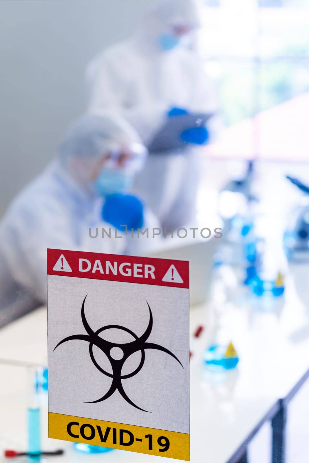 Caution danger Signage of COVID-19 coronavirus in front of Laboratory room with background of Scientists working and researching vaccine for ncov-19 virus for world pandemic situation.