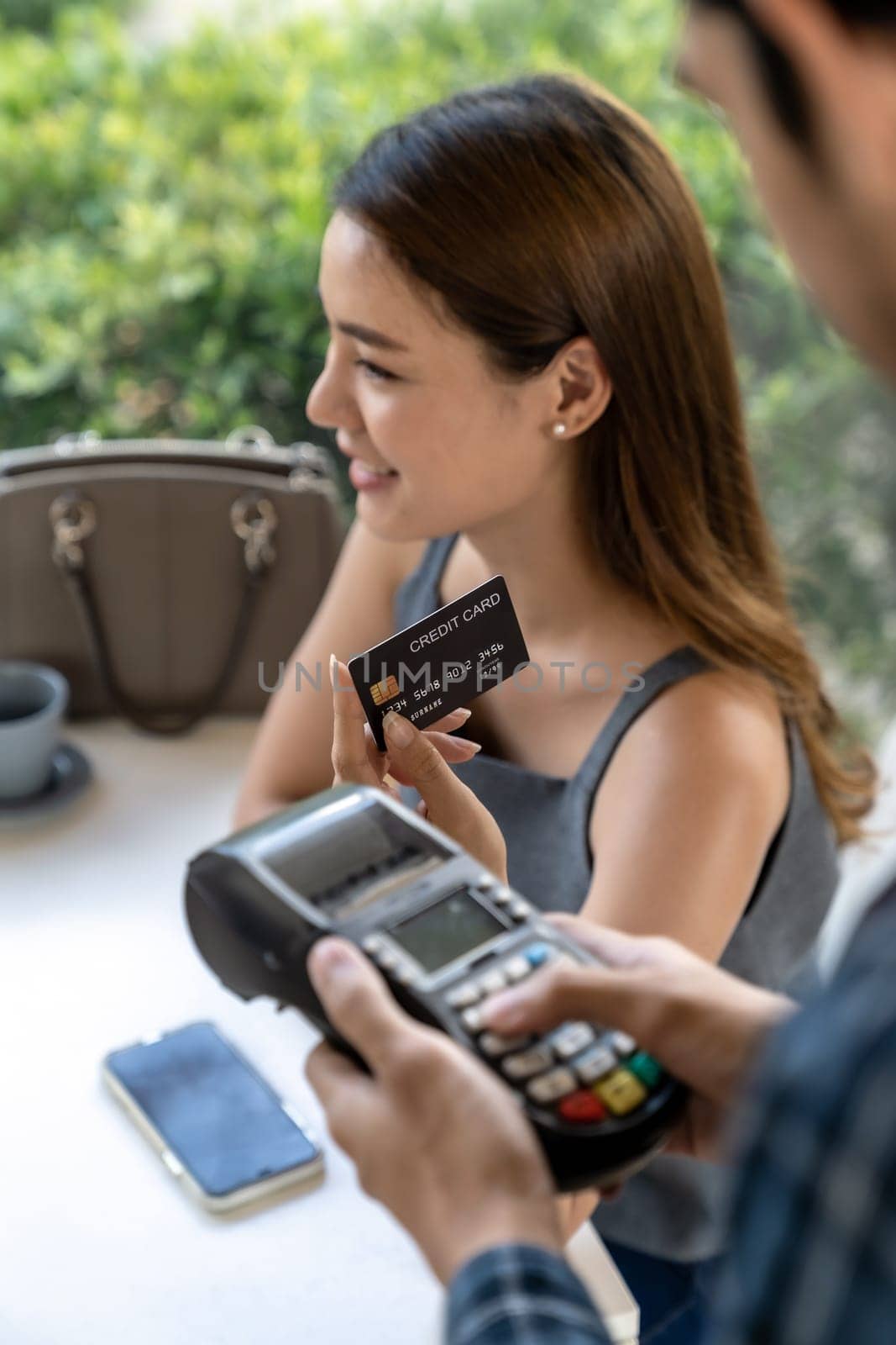 Asian woman customer hold contactless credit card for making online payment after eating out in new normal social distance restaurant. Online contactless and technology concept.