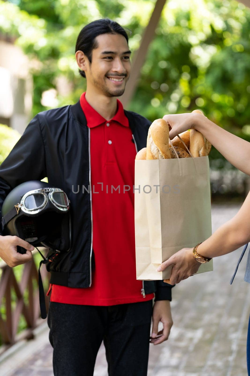 Asian delivery man pick up bakery grocery bag from bakery shop to deliver to customer who make online order. Online food delivery service concept in new normal after coronavirus pandemic.