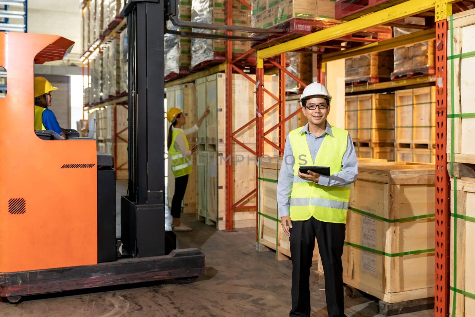 Portrait of Asian warehouse manager hold digital tablet with warehouse worker operate forklift to check inventory in background. Reopening business warehouse technology and logistic concept.