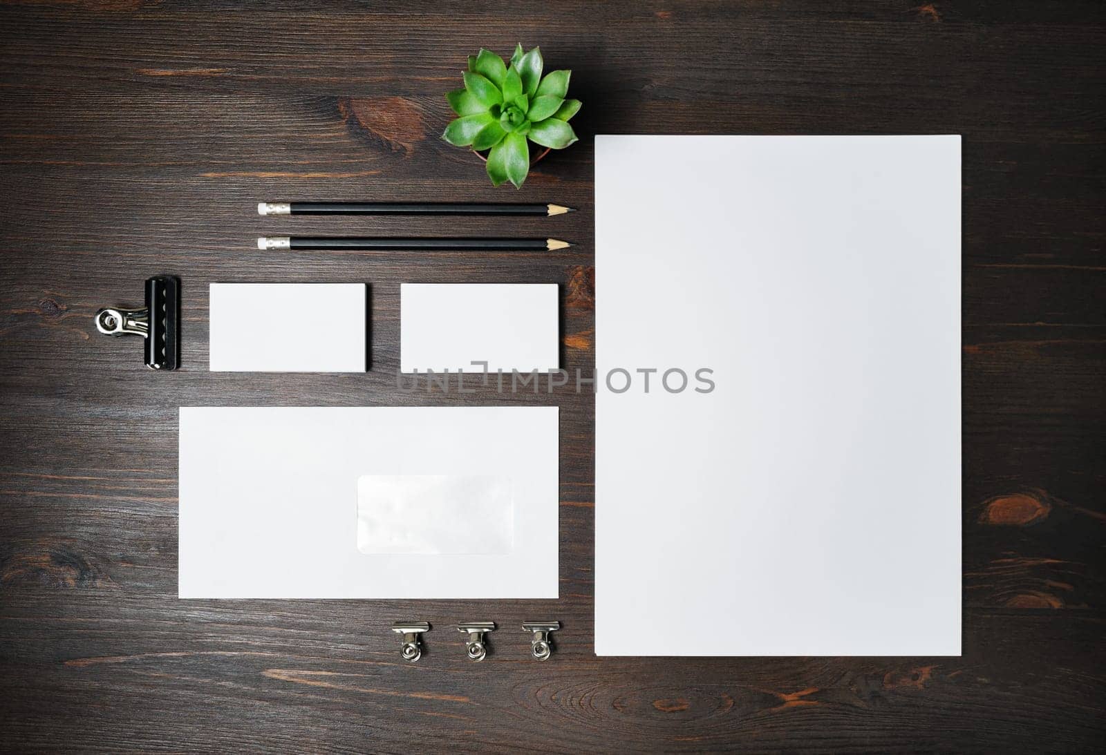 Blank stationery set on wood table background. Envelope, business cards, pencils, plant and A4 paper. Corporate identity template. Responsive design mockup. Flat lay.