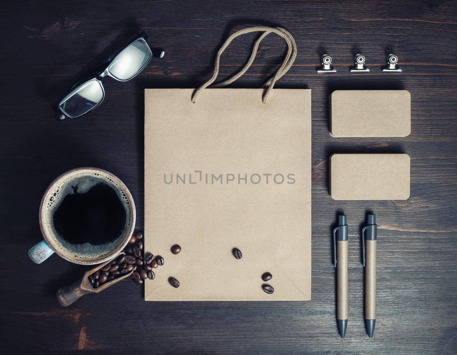 Stationery set. Blank kraft paper bag, business cards. coffee cup, coffee beans and pens on wood kitchen table background. Flat lay.