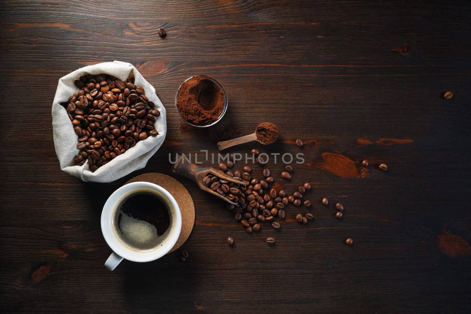 Still life with coffee. Cup of coffee, roasted coffee beans in a sack and ground powder on wooden kitchen table background. Flat lay.