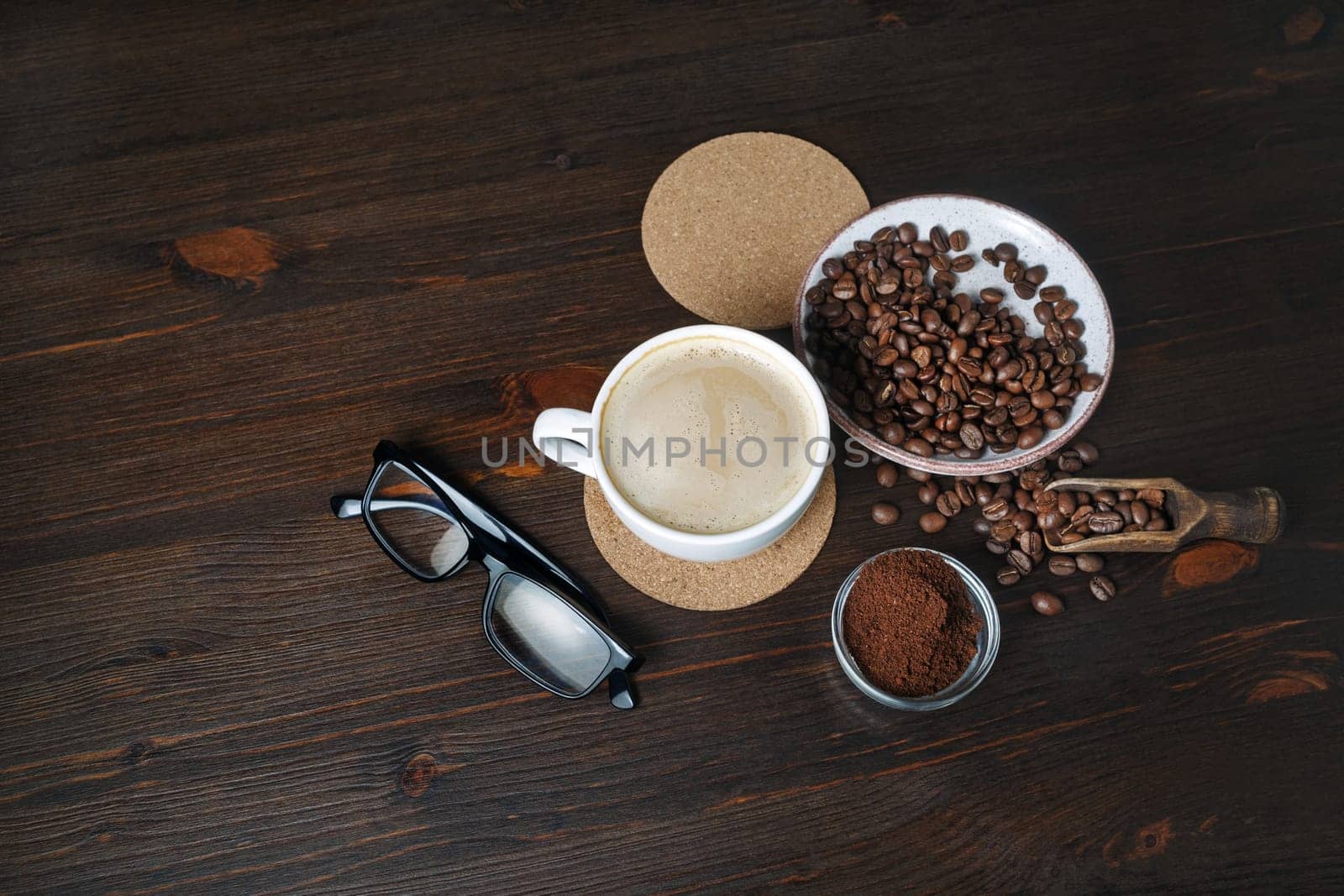 Photo of making coffee. Coffee cup, coffee beans, ground powder, beer coaster and glasses on wood table background.