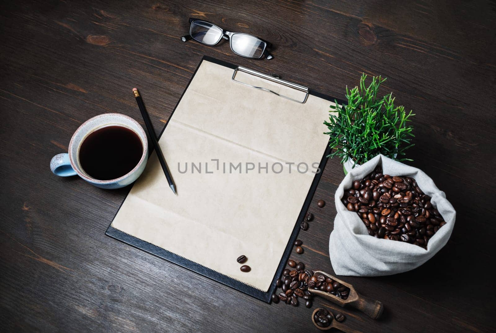 Coffee and blank menu. Clipboard with blank kraft letterhead, coffee cup, coffee beans, plant, glasses and pencil on wood table background.