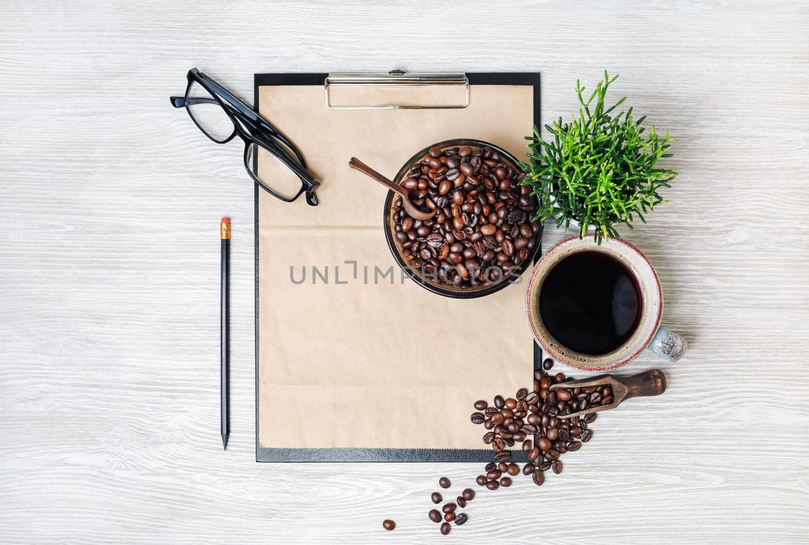 Stationery set and coffee. Clipboard with kraft sheet of paper, coffee cup, coffee beans, pencil, glasses and plant on light wooden background. Flat lay.