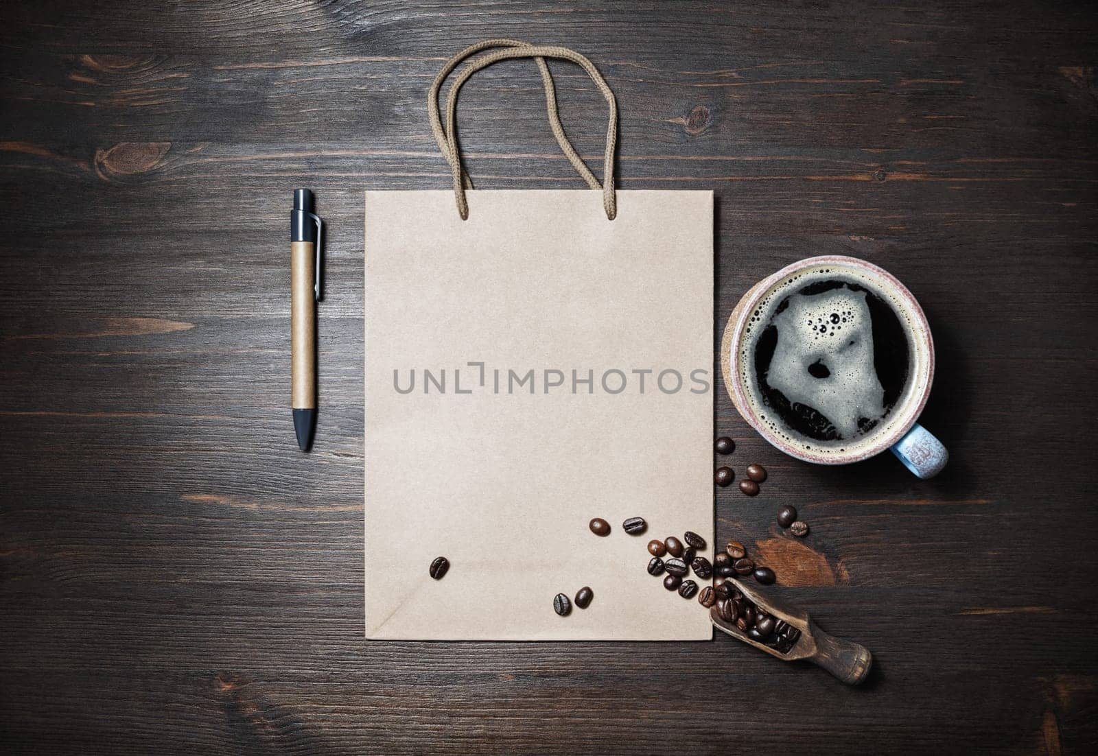 Blank kraft paper bag, coffee cup, coffee beans and pen on wooden background. Space for text. Flat lay.