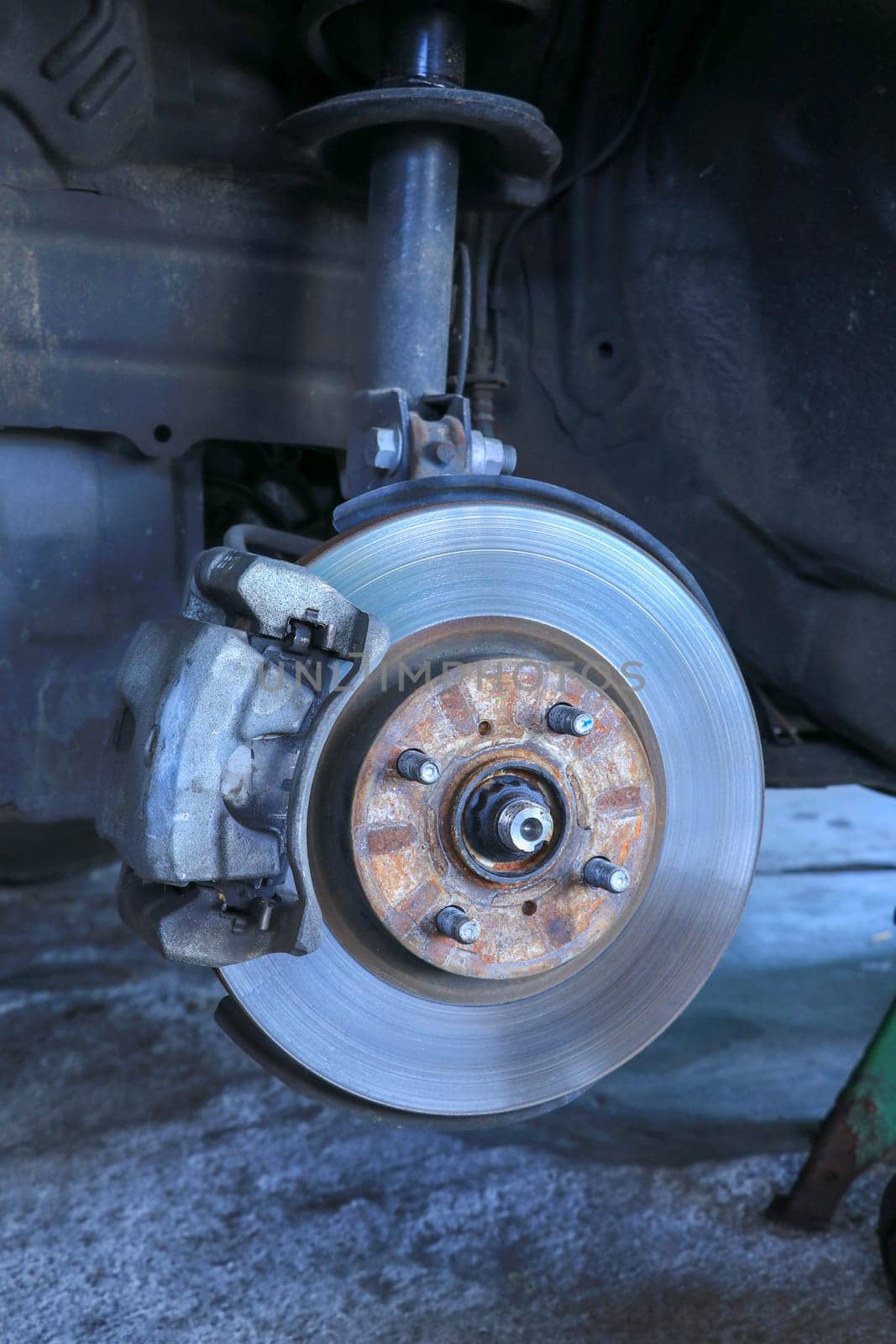 Front disc brake on car in process of new tire replacement. The rim is removed showing the front rotor and caliper.