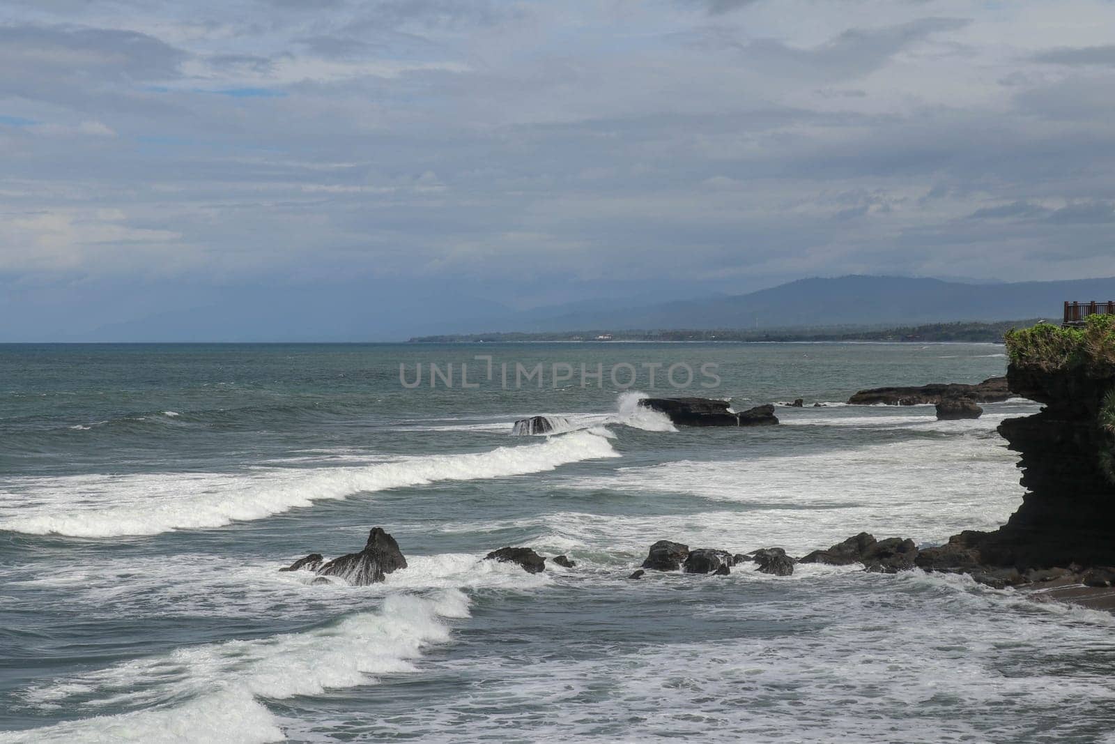 Rock cliffs in the Indian Ocean off the coast of Bali island, near Batu Bolong and tourism attraction spot Tanah Lot temple. Waves are shattering on rocks of solidified black volcanic lava. Indonesia.