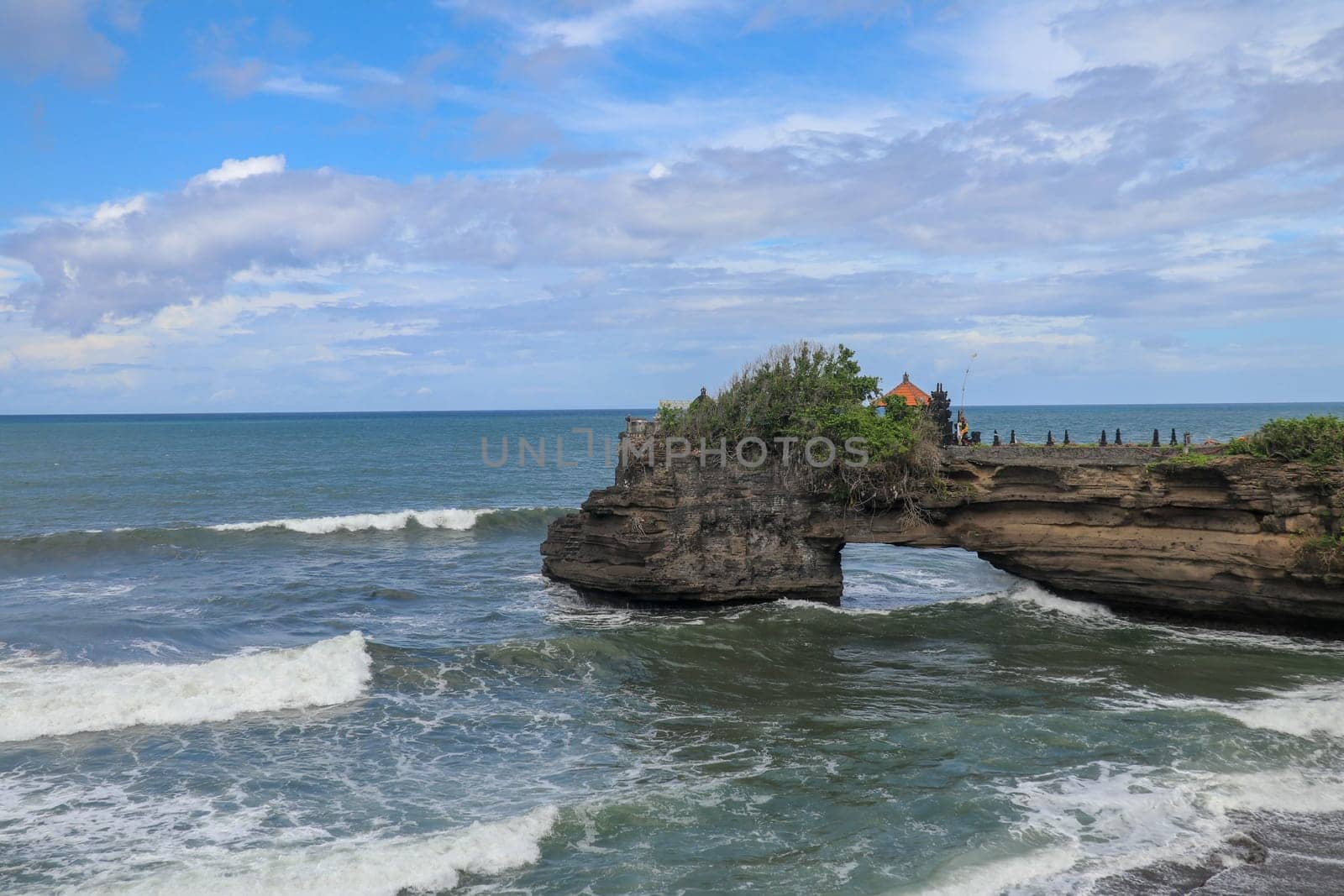 Waves arrive at a rock cliff below Batu Bolong Temple. Tanah Lot temple. Huge hole in rock cliff below Pura Batu Bolong temple. Hindu Temple on the Beatiful Rock in the morning light, Bali, Indonesia.