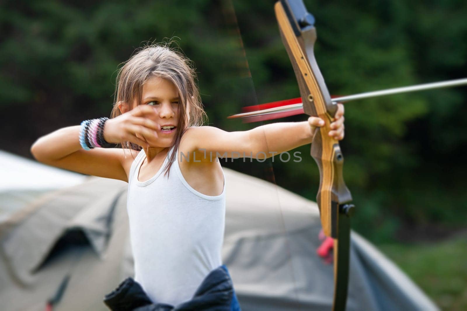 PADIS, BIHOR COUNTY, ROMANIA - AUGUST.25.2016: Happy girl shooting with a bow and arrow in a forest camp with gypsy children