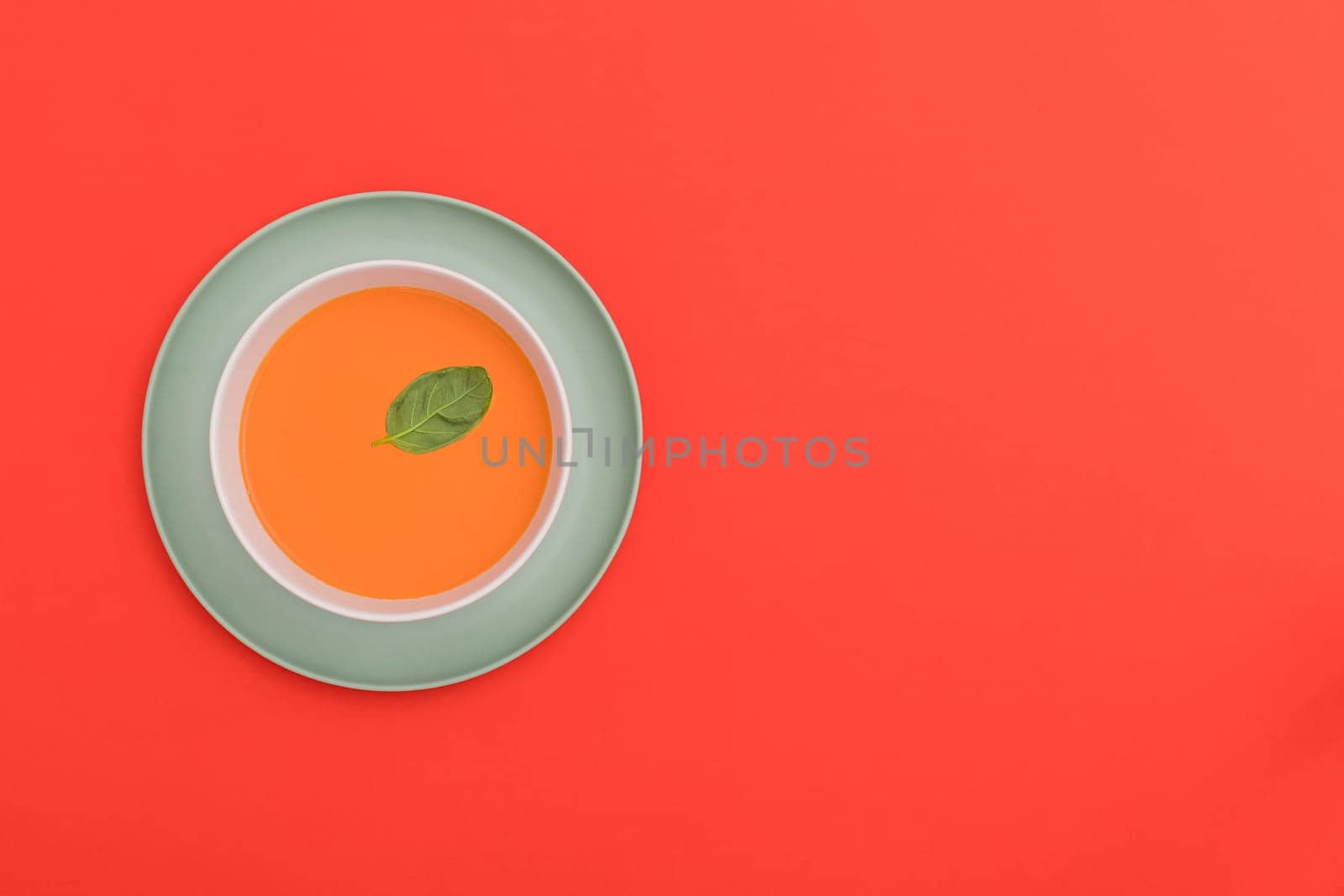 Gazpacho white bowl on a blue plate on red background. Top view. Copy space.