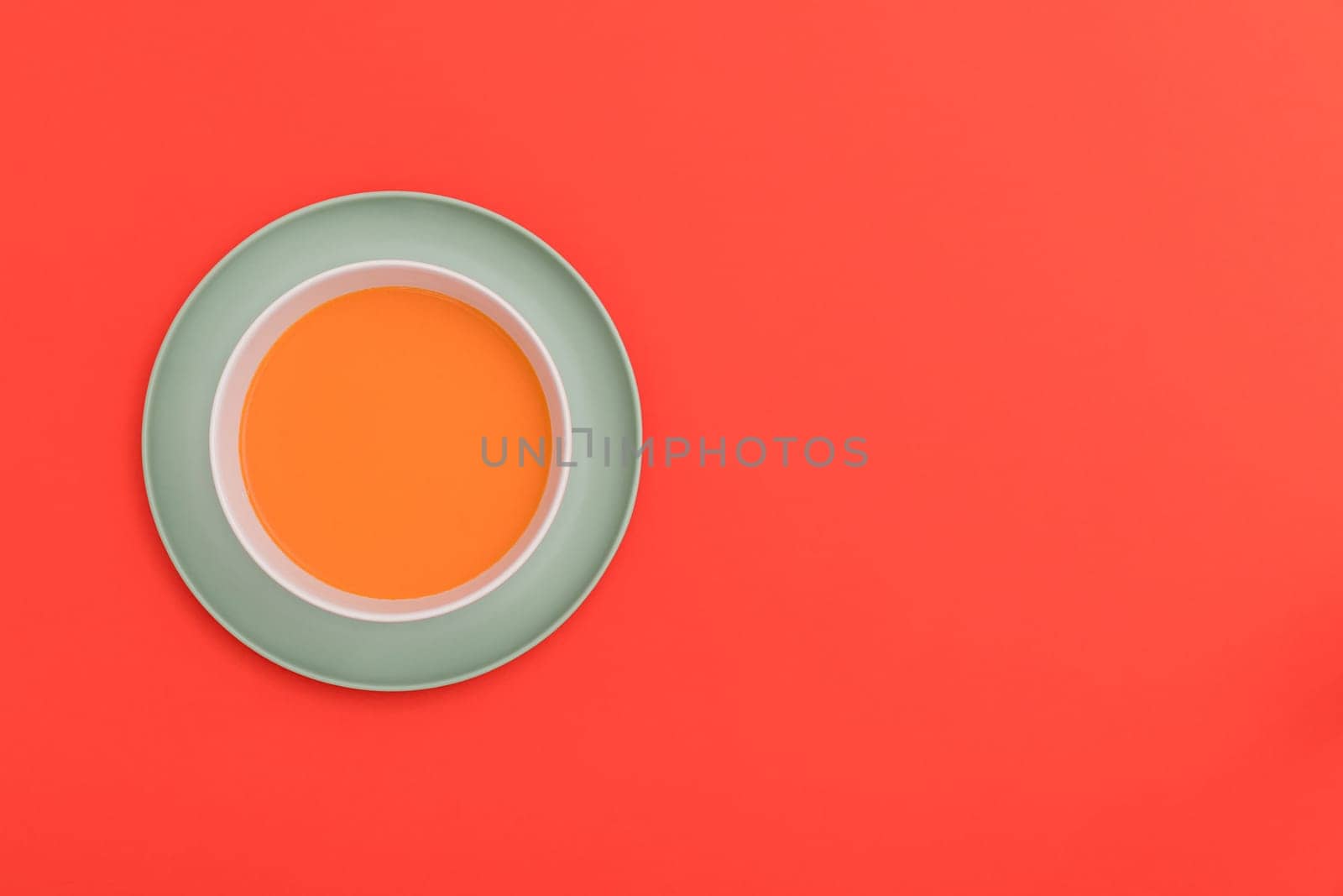 Gazpacho white bowl on a blue plate on red background. Top view. Copy space.