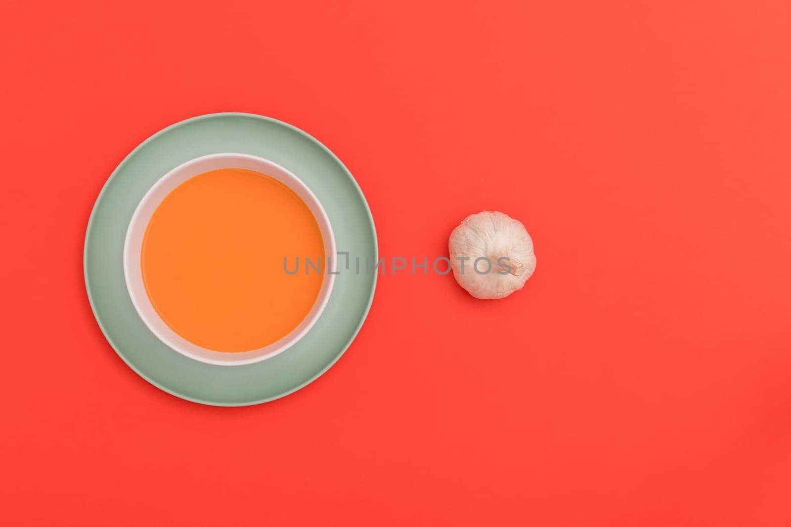 Gazpacho white bowl on a blue plate with a garlic bulb on red background. Top view. Copy space.