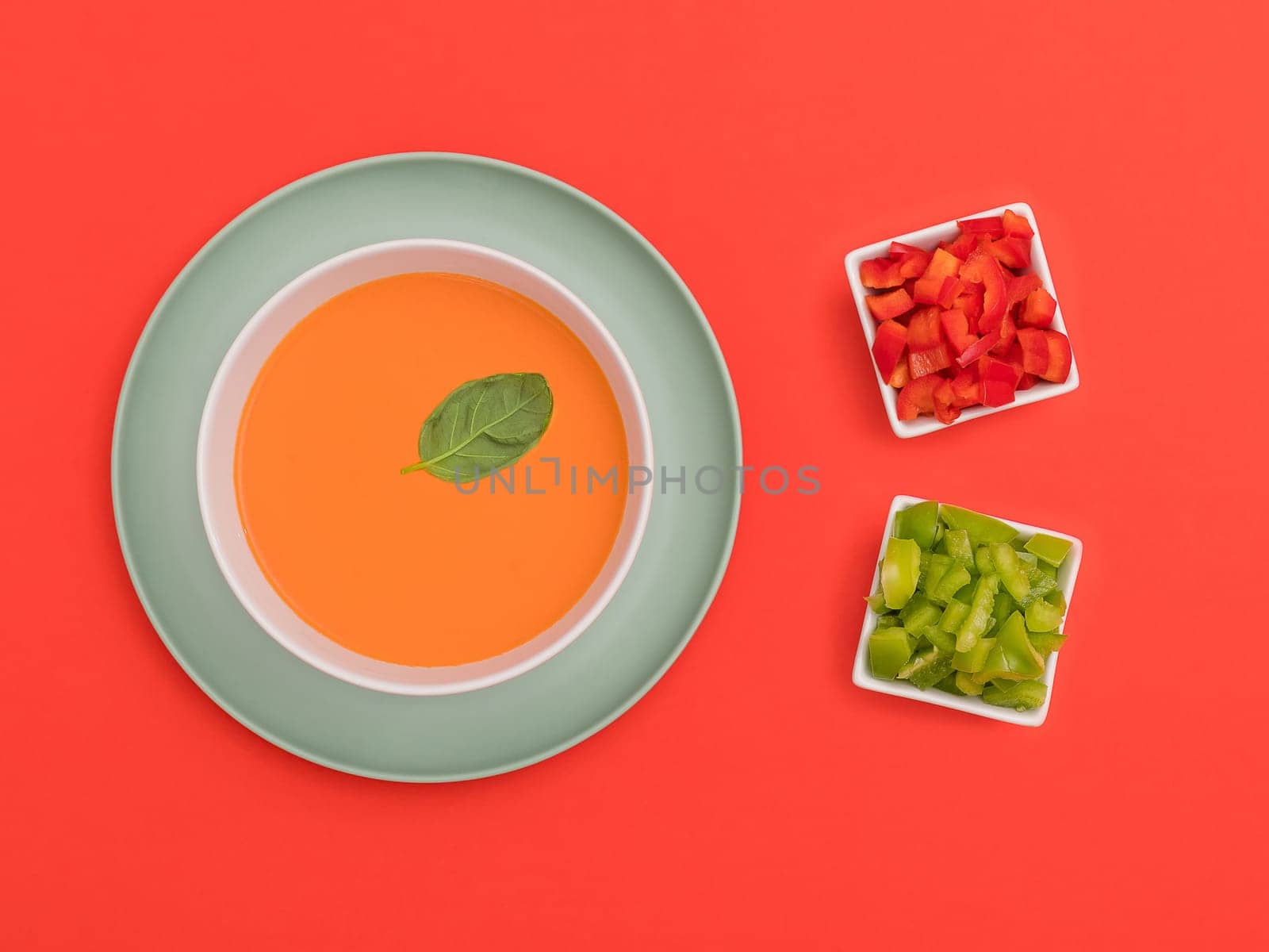 Gazpacho white bowl on a blue plate with red and green peppers on red background. Top view. Copy space.