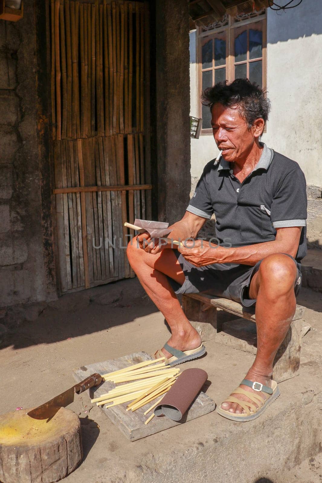 Old man working with bamboo in his workshop to make bamboo straws, Bali, Indonesia. Ecological way of producing recyclable products. Front view to a worker who makes bamboo straws.