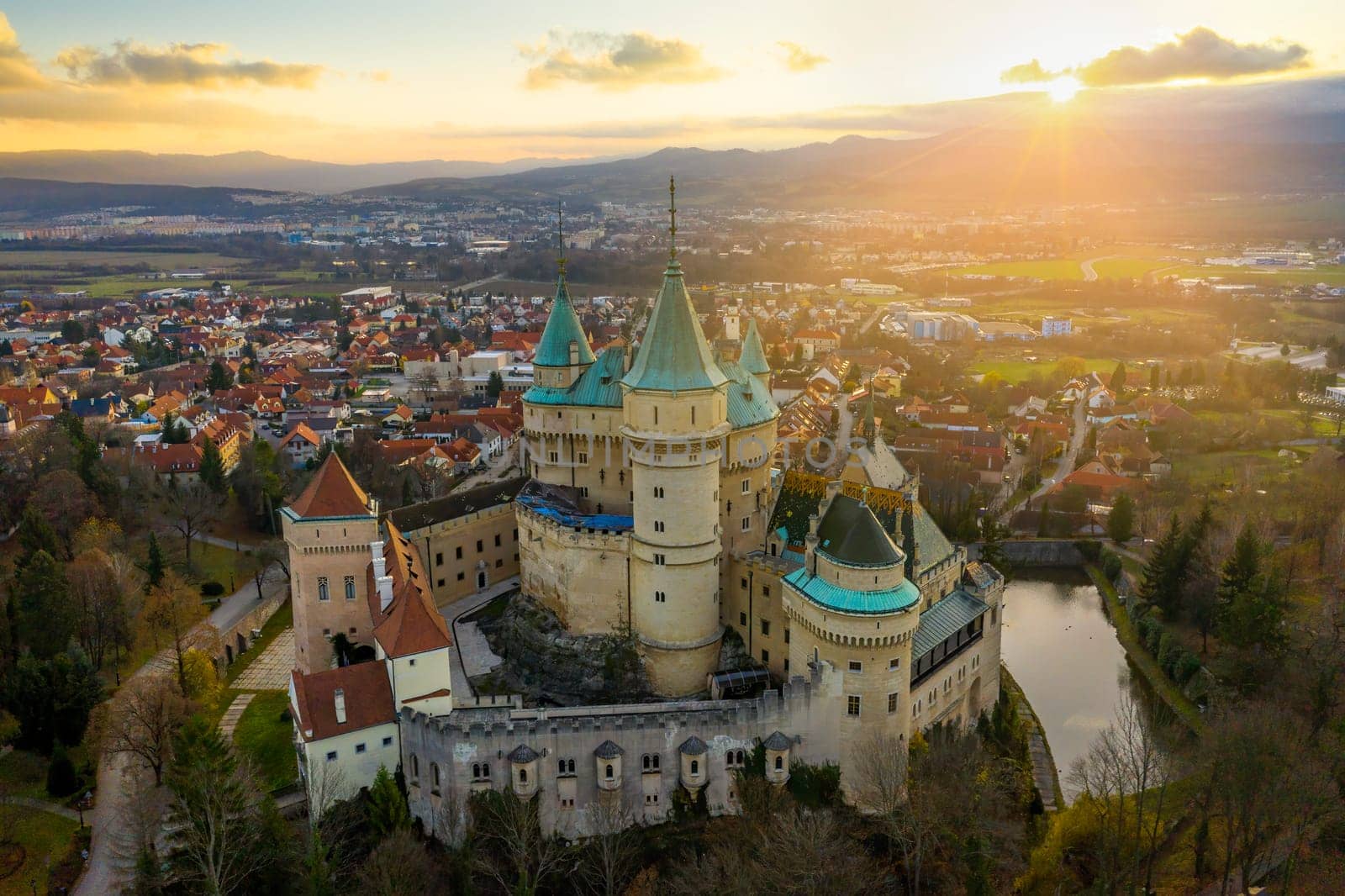 Soft morning sun peeking from behind a cloud and shining down on 12th century medieval Bojnice castle overlooking its namesake town.