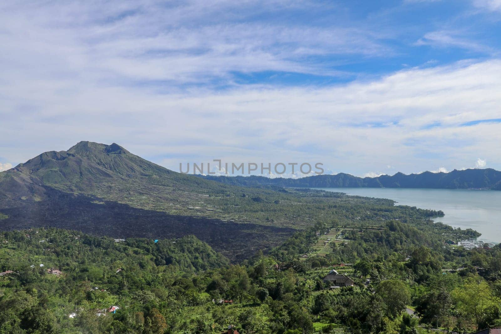 Volcano landscape with lava fields, pine tree forest and farms and houses on the slopes. Kintamani is a village on the western edge of the larger caldera wall of Gunung Batur in Bali, Indonesia.