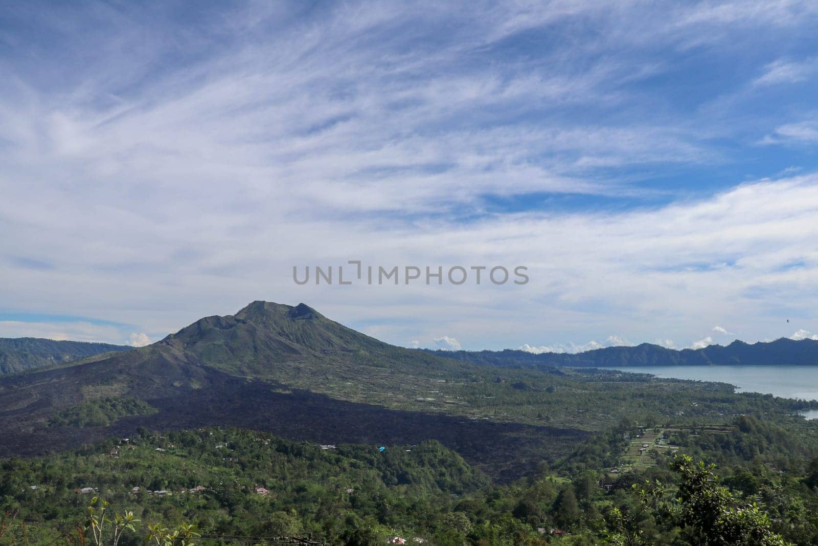 Volcano landscape with lava fields, pine tree forest and farms and houses on the slopes. Kintamani is a village on the western edge of the larger caldera wall of Gunung Batur in Bali, Indonesia.