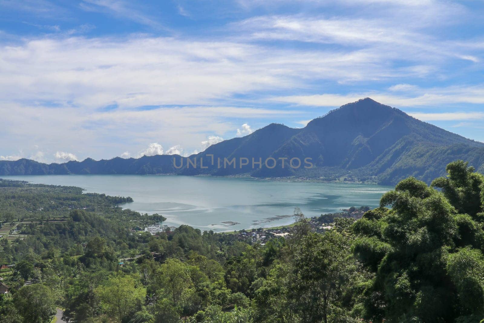 Mountain lake in the volcanic caldera of Batur under Mount Abang on the island of Bali, Indonesia. Quiet level of a large drinking water reservoir. High mountain peaks rise above the lake. Blue sky.