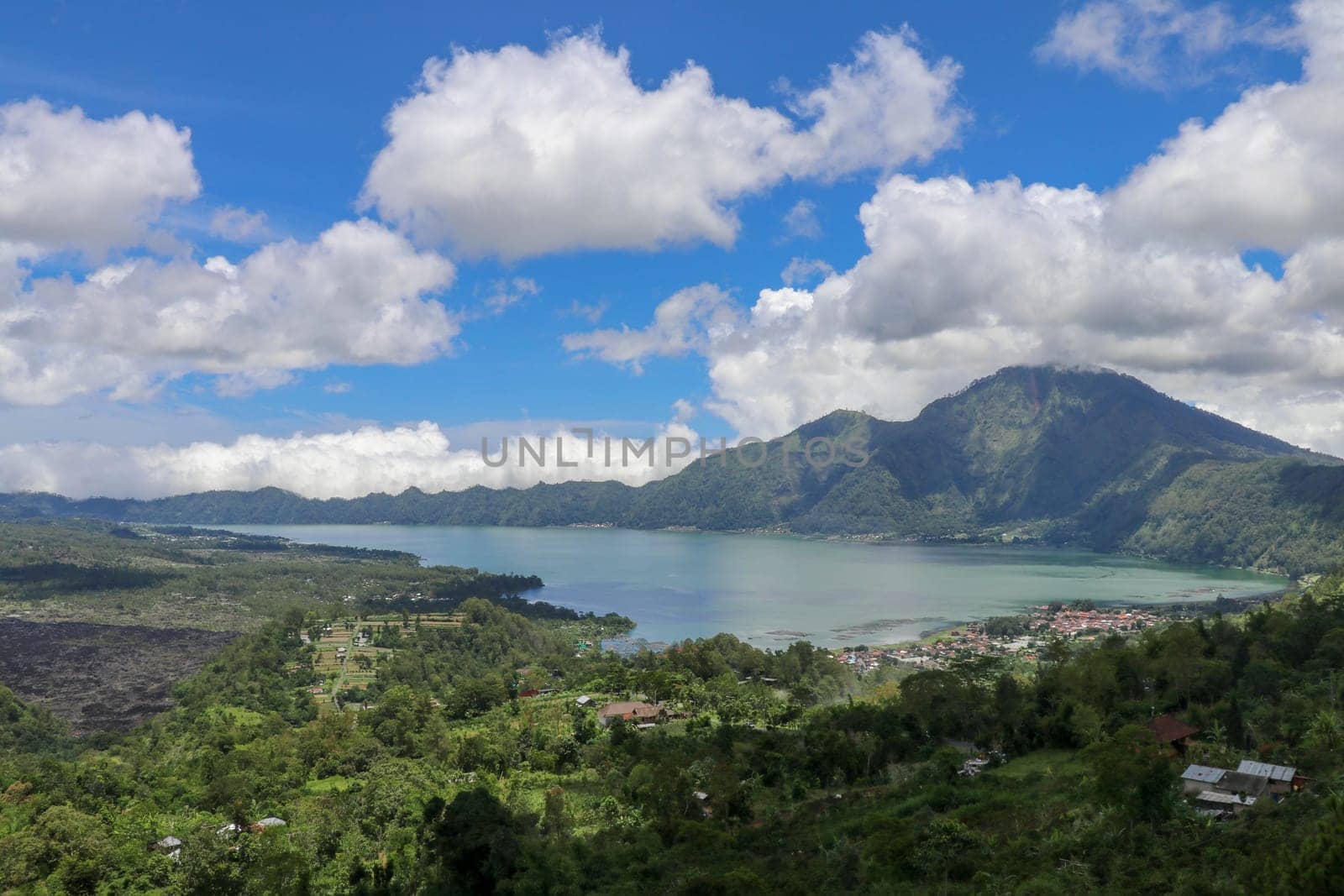 Mountain lake in the volcanic caldera of Batur under Mount Abang on the island of Bali, Indonesia. Quiet level of a large drinking water reservoir. High mountain peaks rise above the lake. Blue sky.