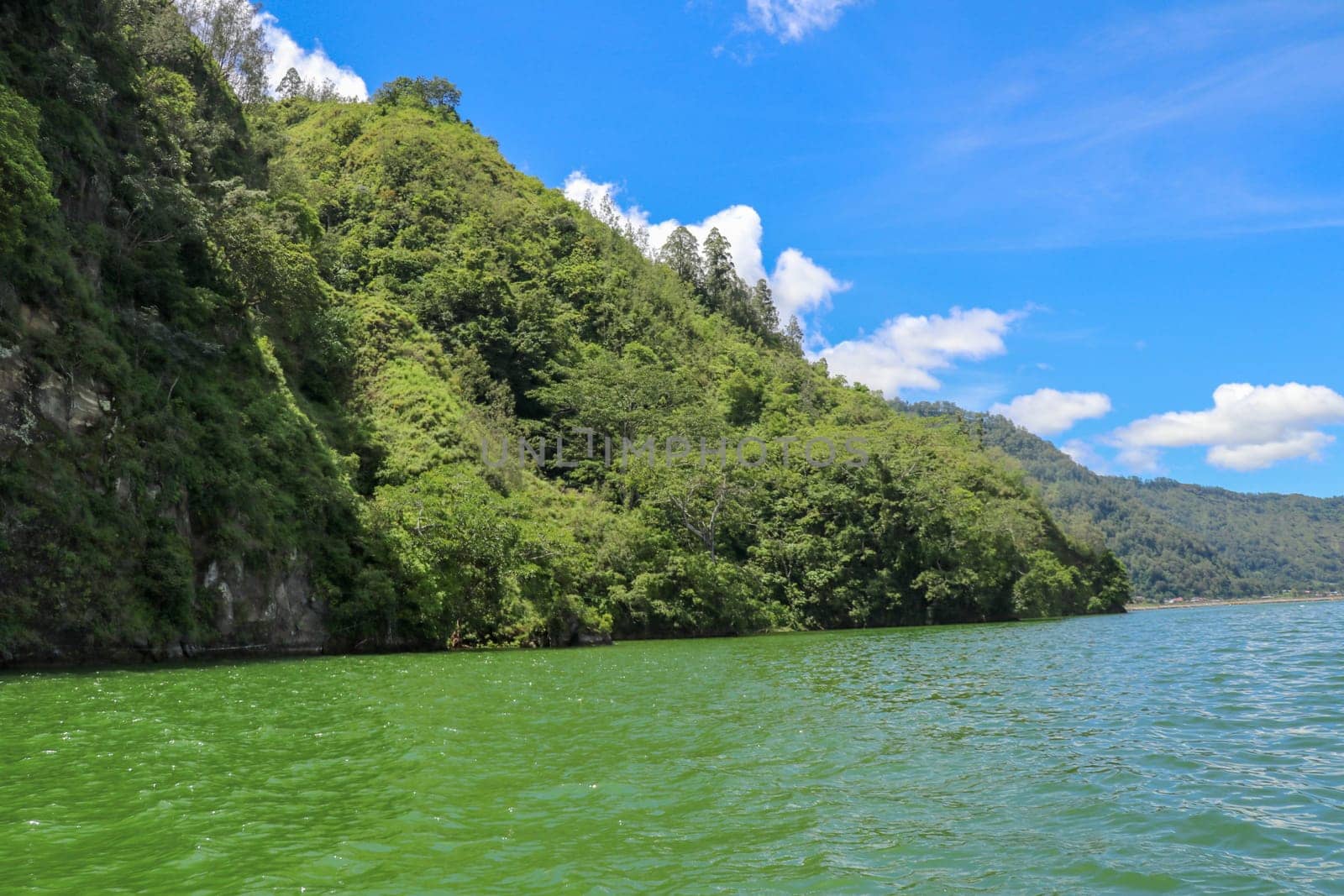 Sailing a traditional fishing boat from the village of Trunyan to a unique cemetery. High mountains covered with dense tropical vegetation line the coast of Lake Batur on the island of Bali, Indonesia