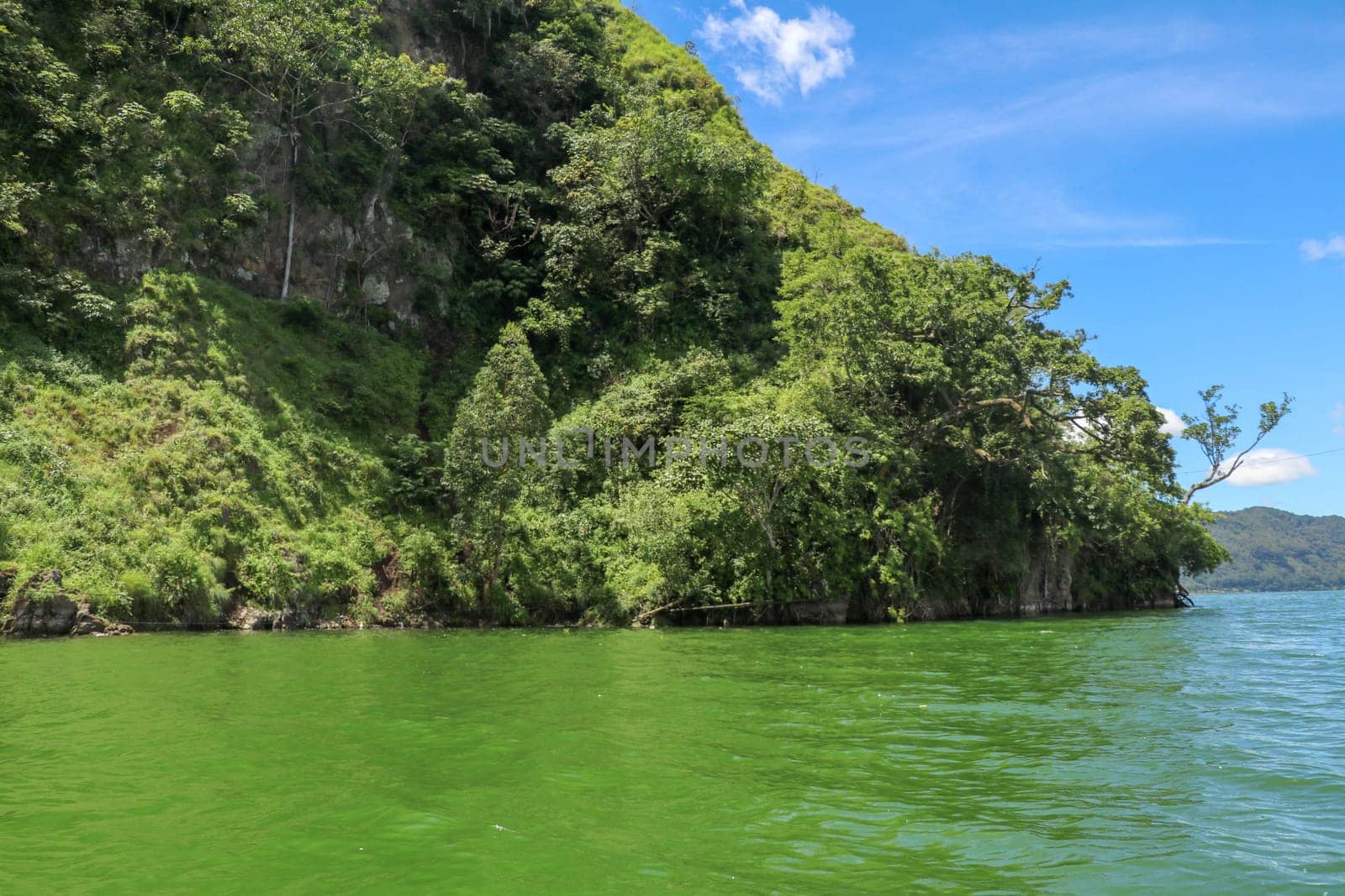 Sailing a traditional fishing boat from the village of Trunyan to a unique cemetery. High mountains covered with dense tropical vegetation line the coast of Lake Batur on the island of Bali, Indonesia