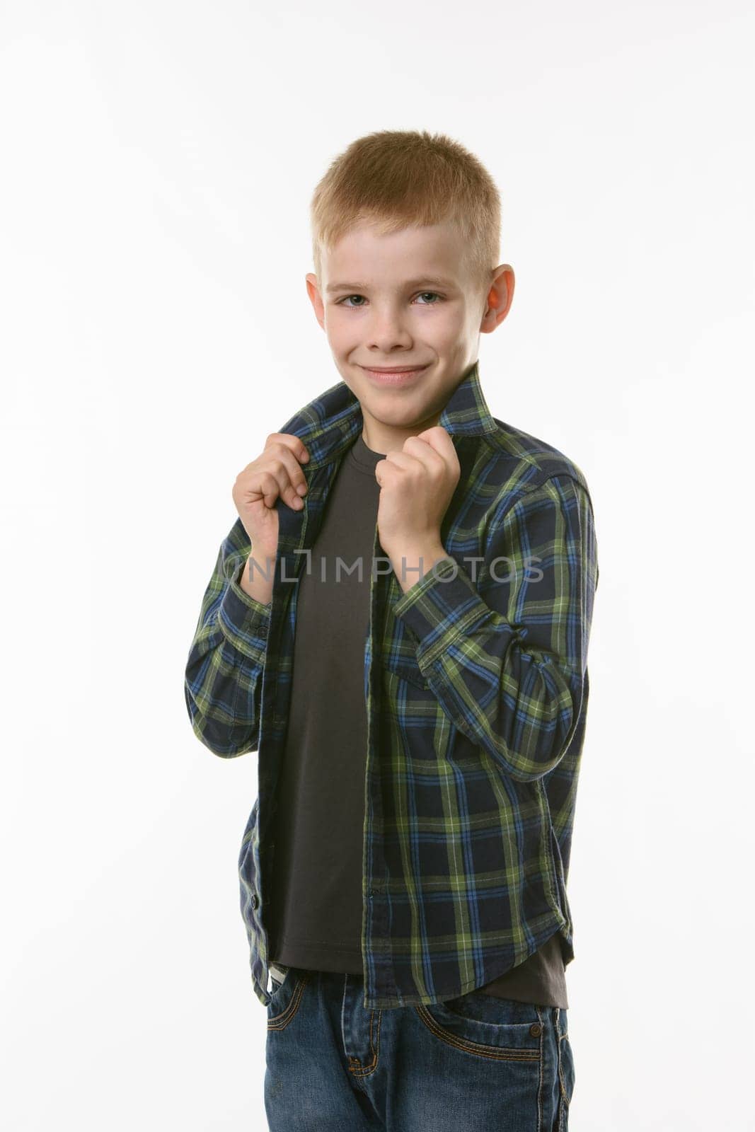 blond boy on a white background holds hands behind the collar of a checkered shirt