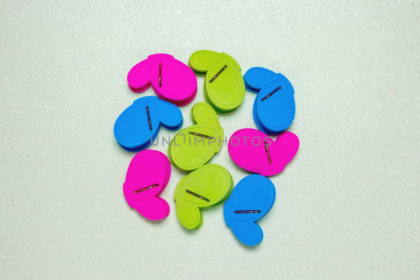 Colourful set of nine plastic clothespins or pegs on a light green sparkling background with copy field. View from above.