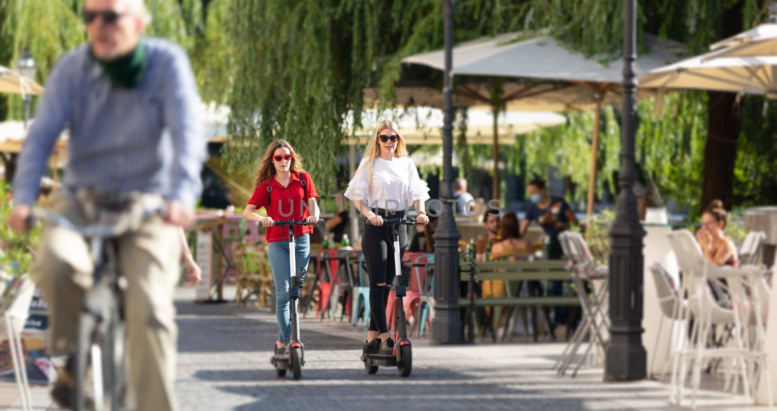 Trendy fashinable teenager girls riding public rental electric scooters in urban city environment. New eco-friendly modern public city transport in Ljubljana, Slovenia.