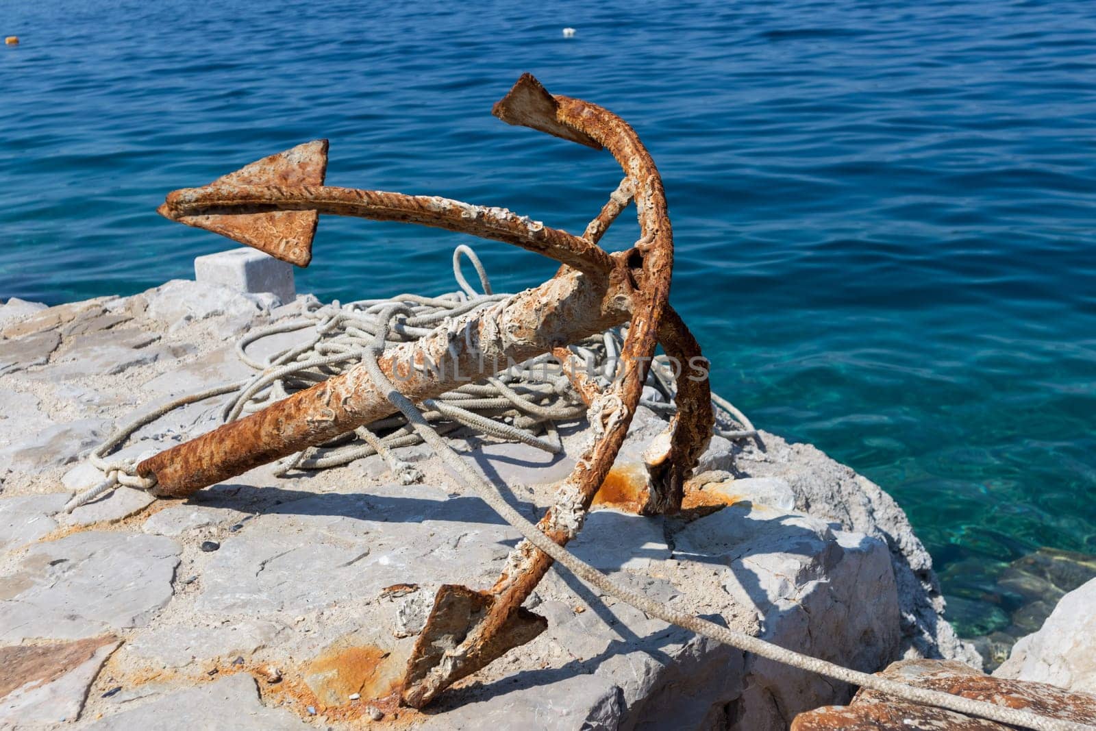Old rusty anchor on rock by blue adriatic sea.